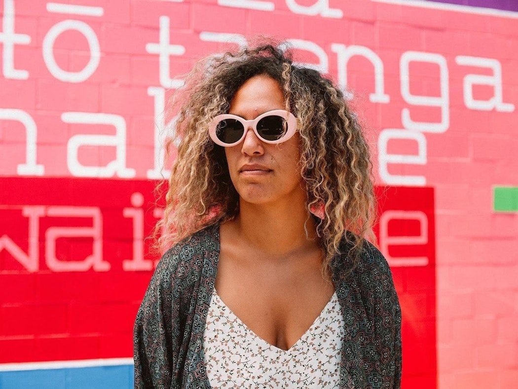 A person wearing pink sunglasses standing against a pink and red painted background